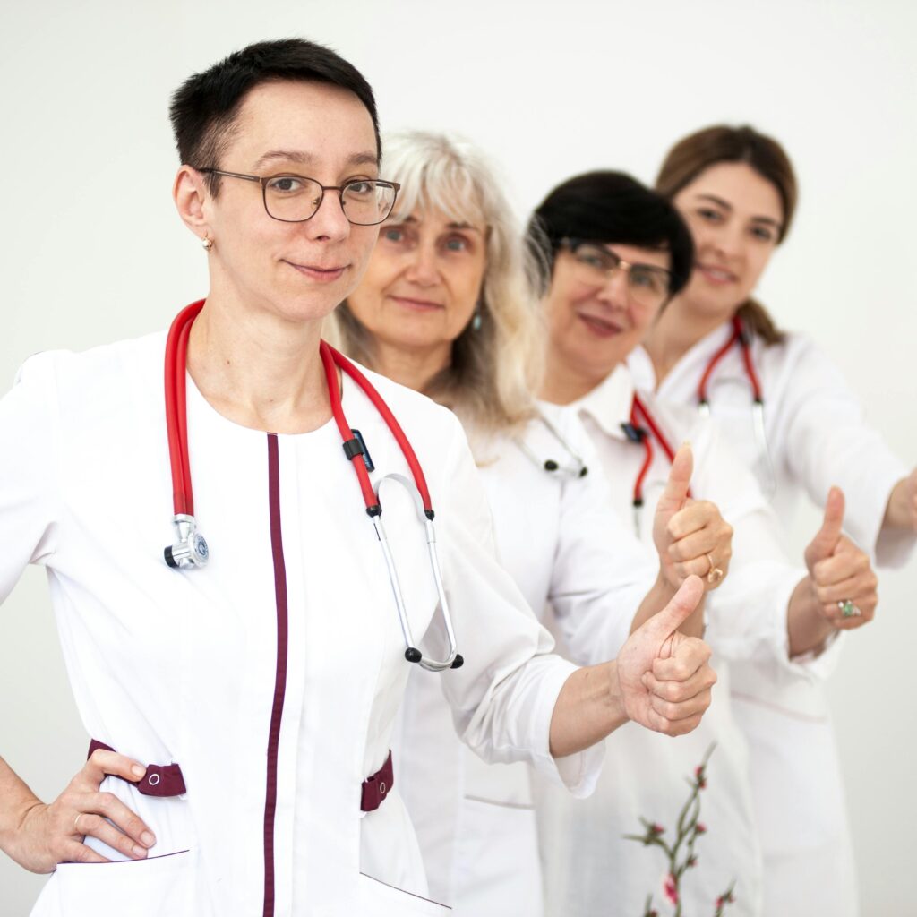 A group of female doctors in white coats showing thumbs up, symbolizing teamwork and women empowerment in healthcare.